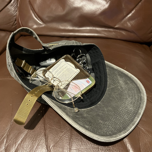 Grey hat upside down with keys, wallet, glasses, and watch inside